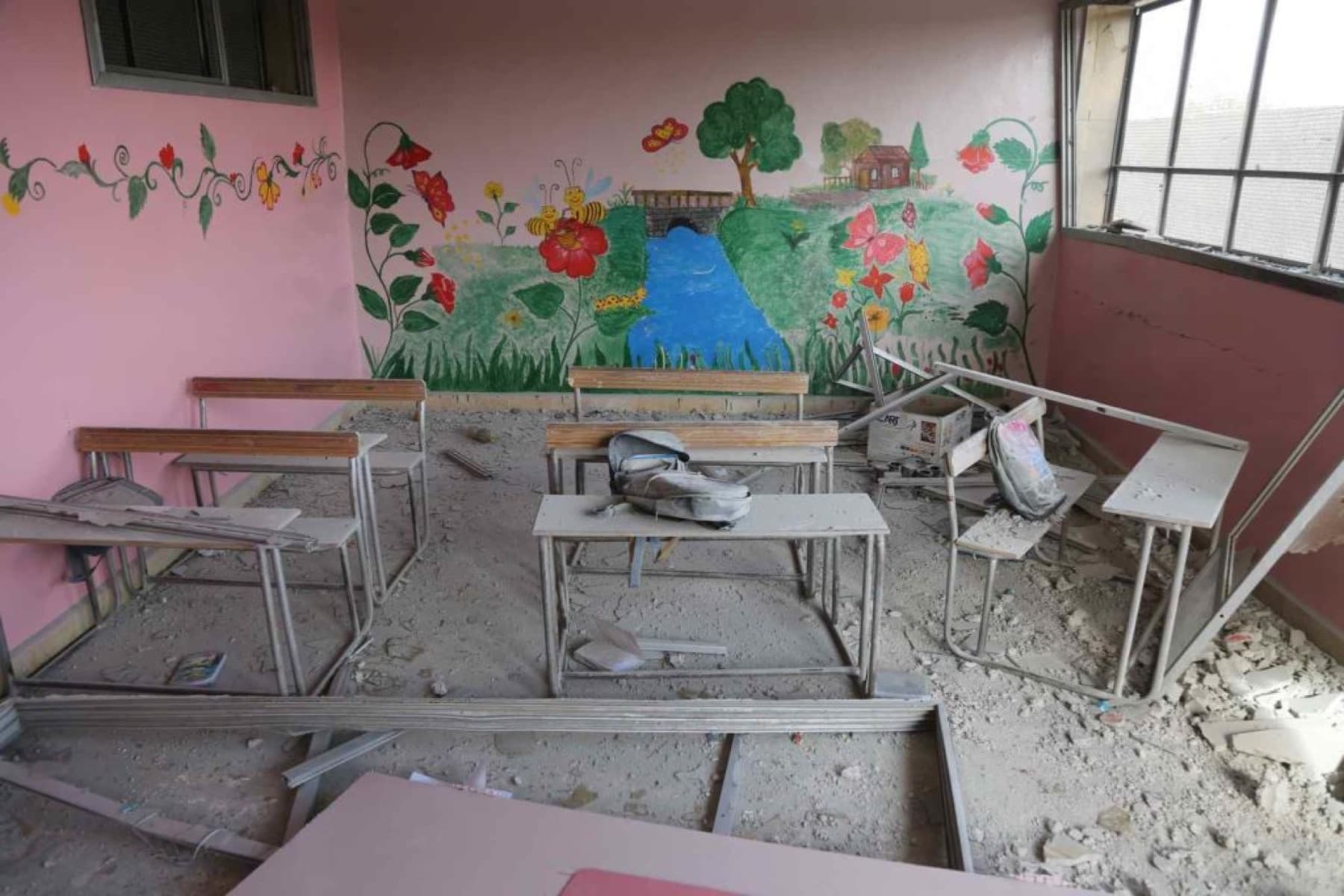 Klassenzimmer mit kindlicher Wandmalerei, Schutt auf dem Boden und umgestürzten Bänken